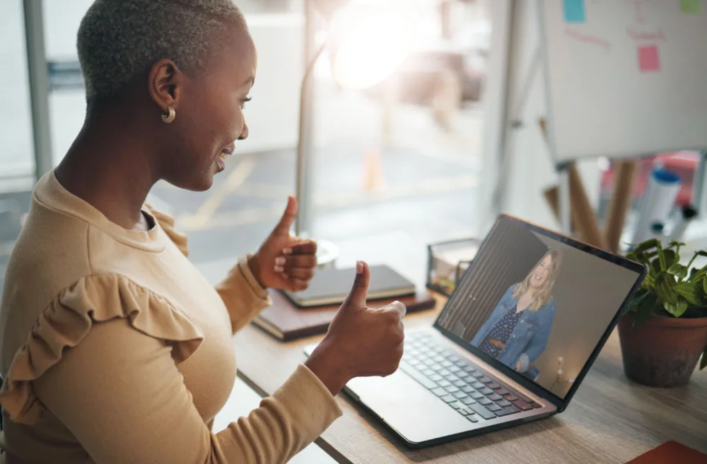 An employee at her desk giving a thumbs up during a video call with Rainbow.