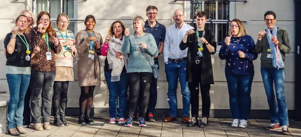 A group of training participants standing outside, smiling and blowing bubbles together.
